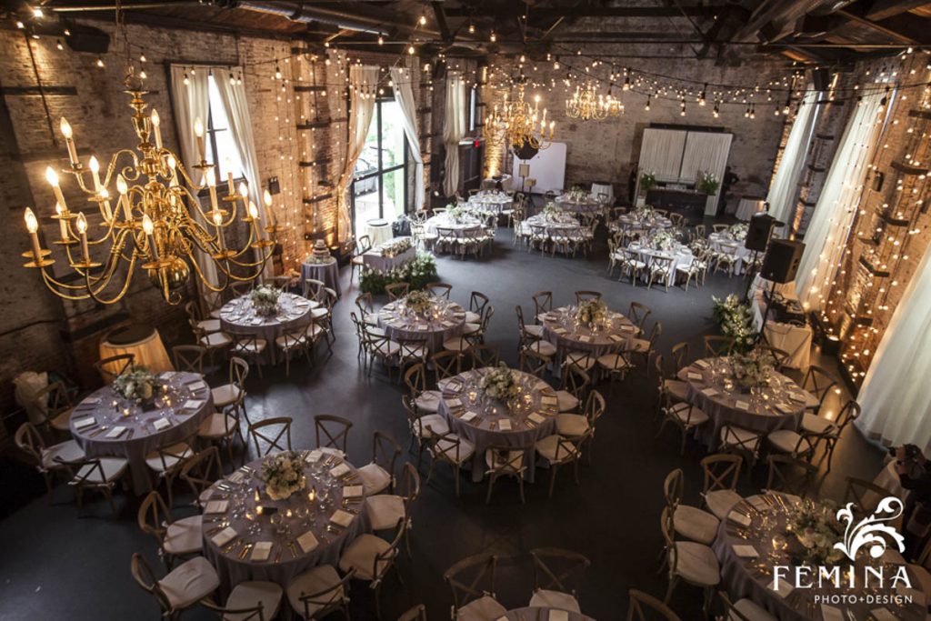 Elegant banquet hall arranged for an event with round tables, chandeliers, and string lights.