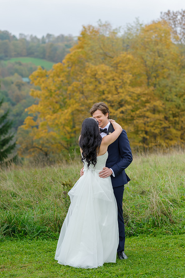 A couple in wedding attire embracing outdoors with a picturesque landscape in the background.