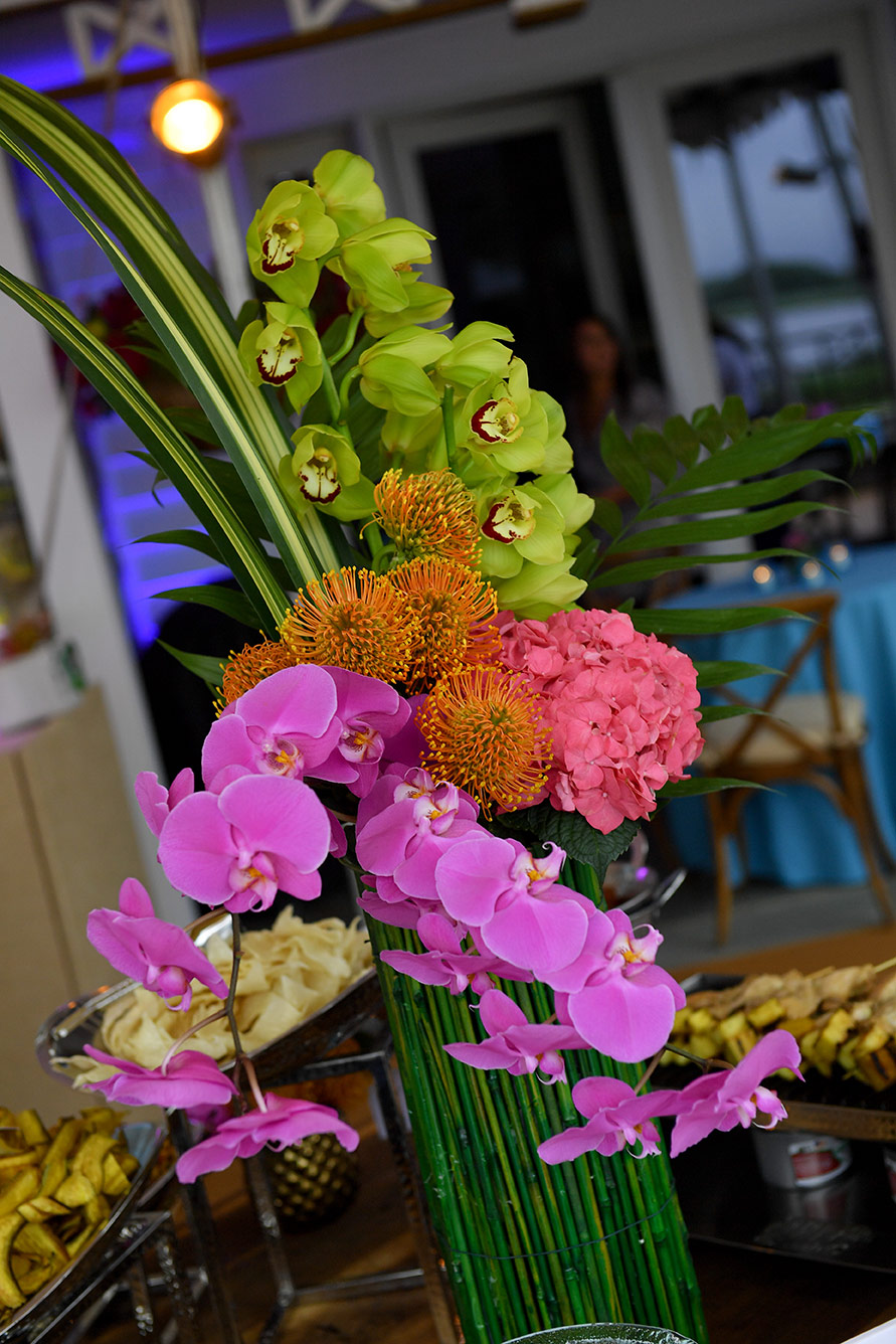 An elaborate floral centerpiece with orchids, pink hydrangeas, and tropical foliage on a table at an event.