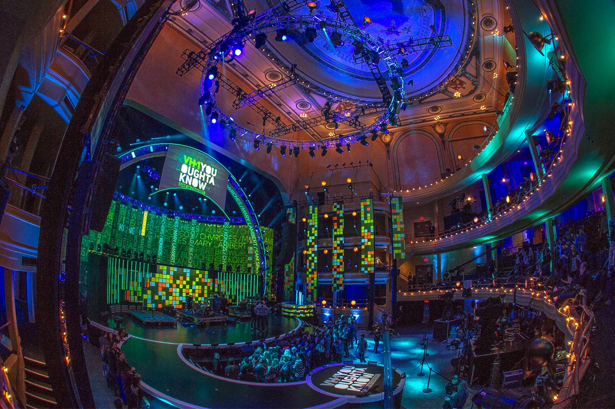 A wide-angle view of a vibrant and modern theater interior during a live event with an audience, featuring a large, illuminated stage with digital screens. A wide-angle view of a vibrant and modern theater interior during a live event with an audience, featuring a large, illuminated stage with digital screens.