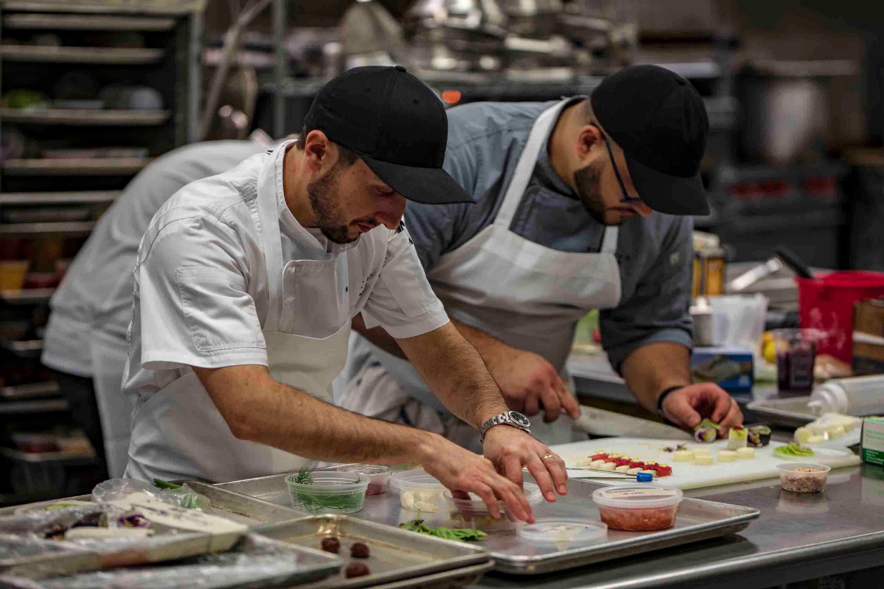 Two chefs focused on carefully plating dishes in a professional kitchen.