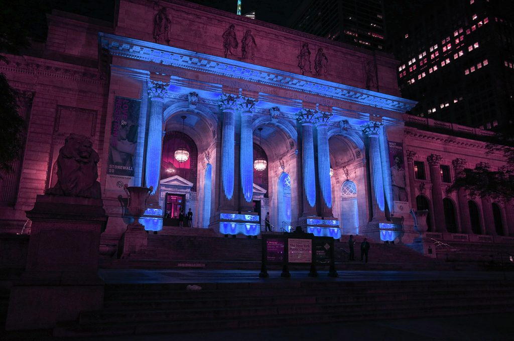 The new york public library lit with blue lights at night.